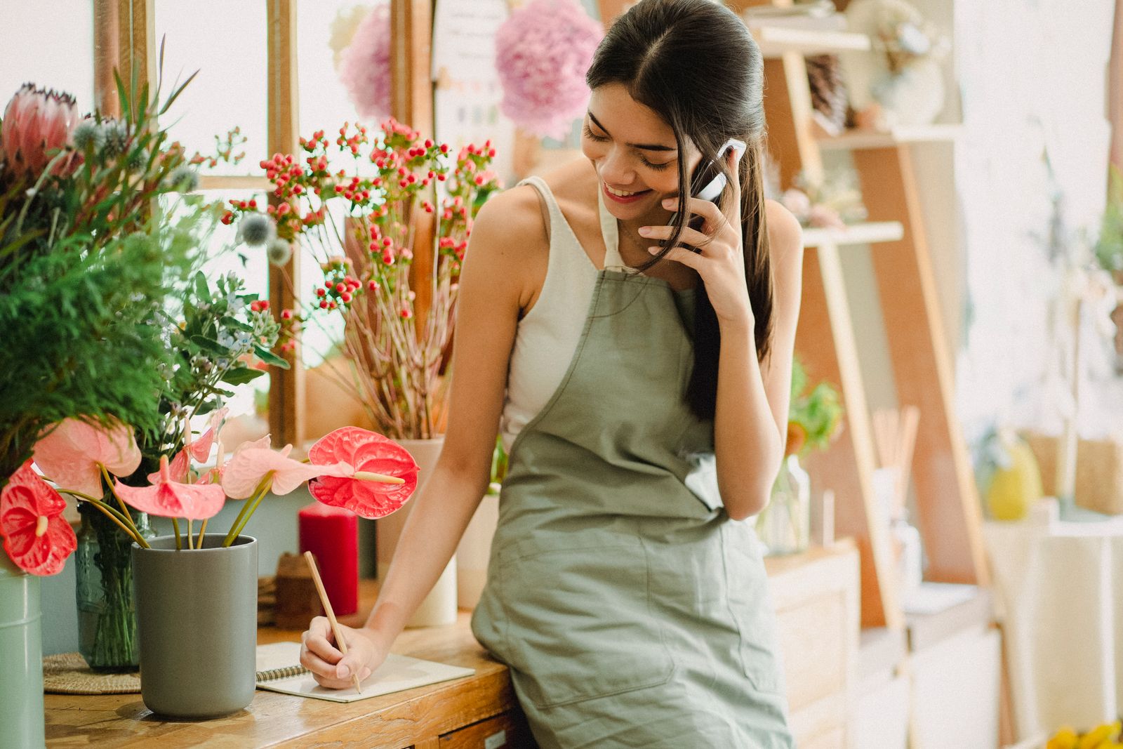 Dona de uma floricultura anotando um pedido enquanto atende o telefone