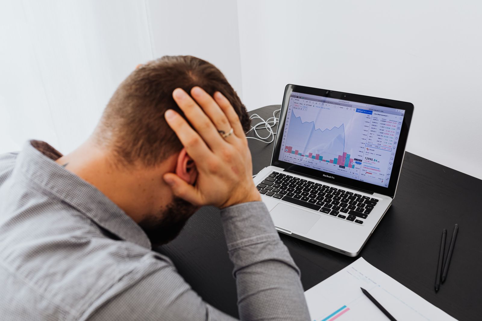 Homem com a cabeça entre as mãos na frente de um notebook mostrando um gráfico em queda