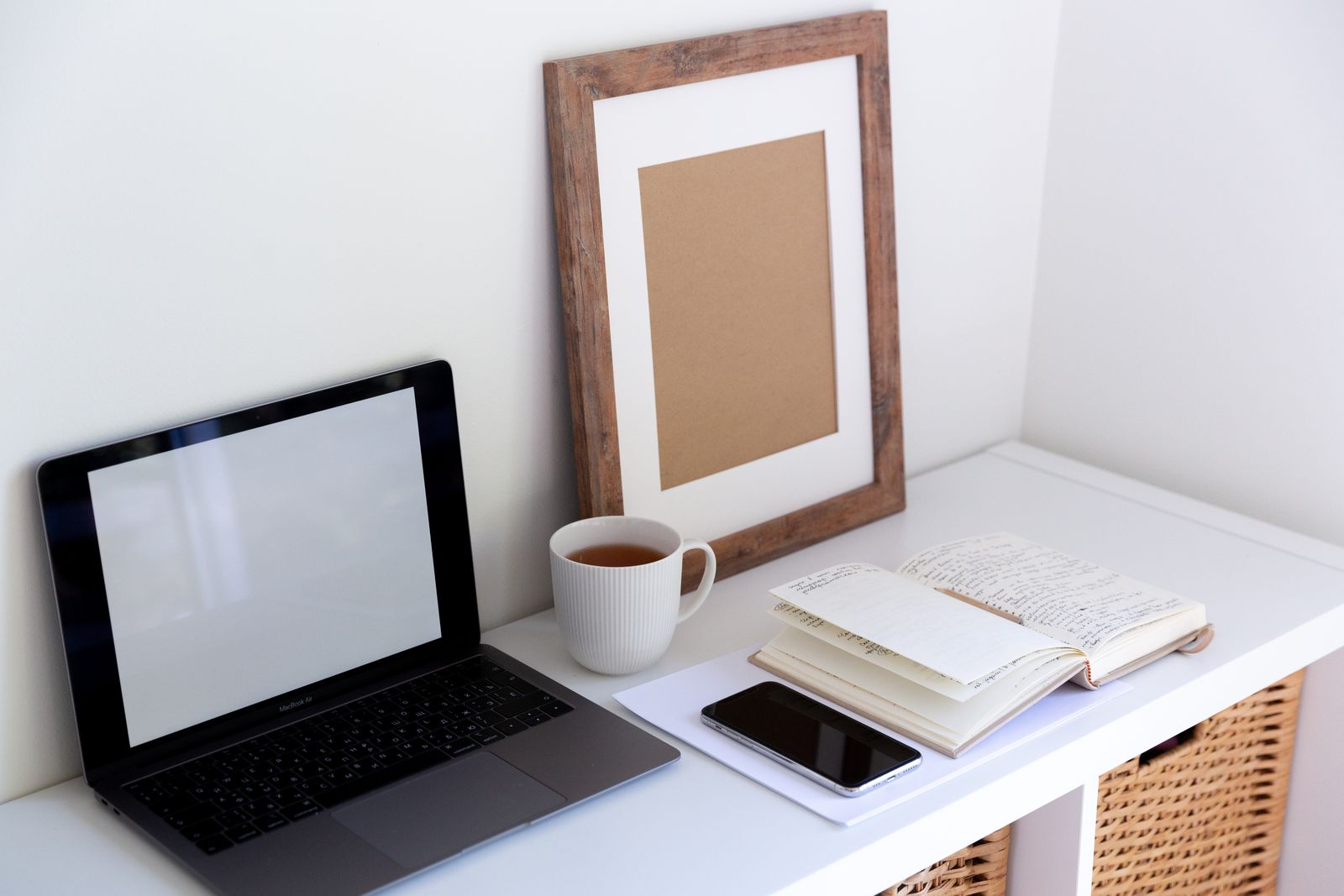 Mesa clara com notebook aberto, caderno, xícara e celular com a tela apagada