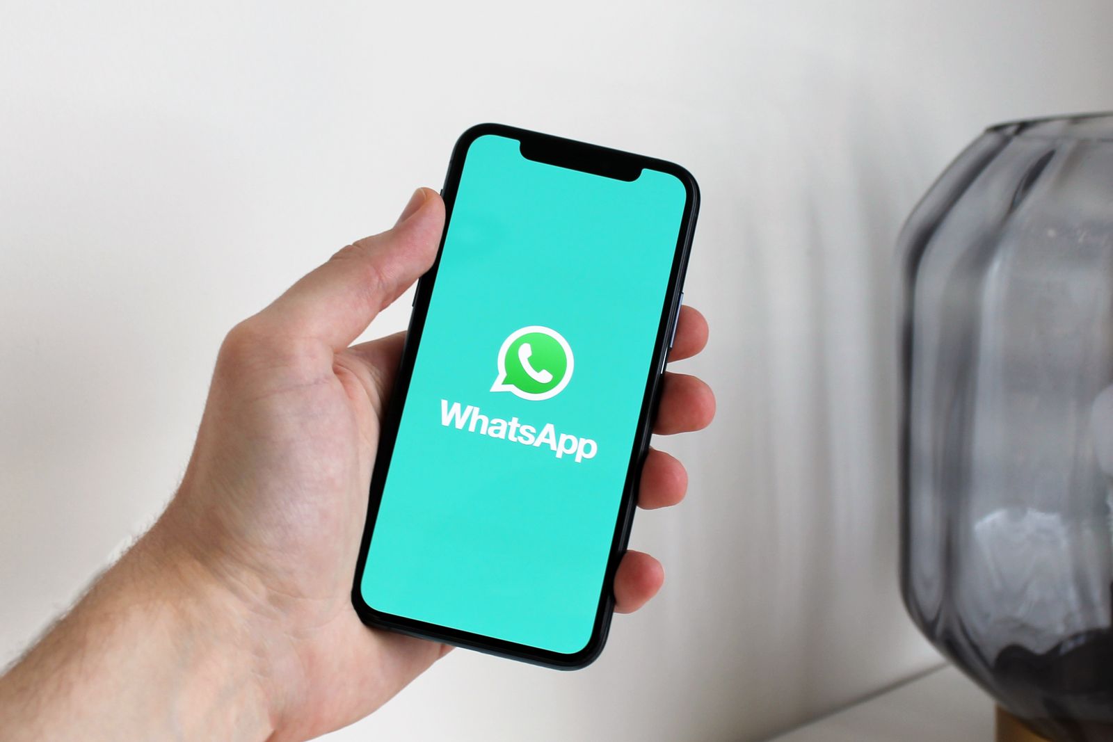 Mão segurando um celular com a tela de abertura do WhatsApp